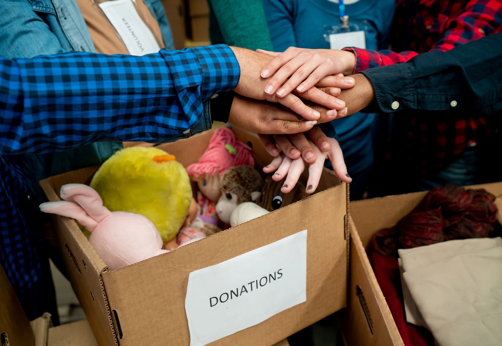 Close up of diverse group of volunteers receiving and organizing donations in boxes all with hands in a huddle