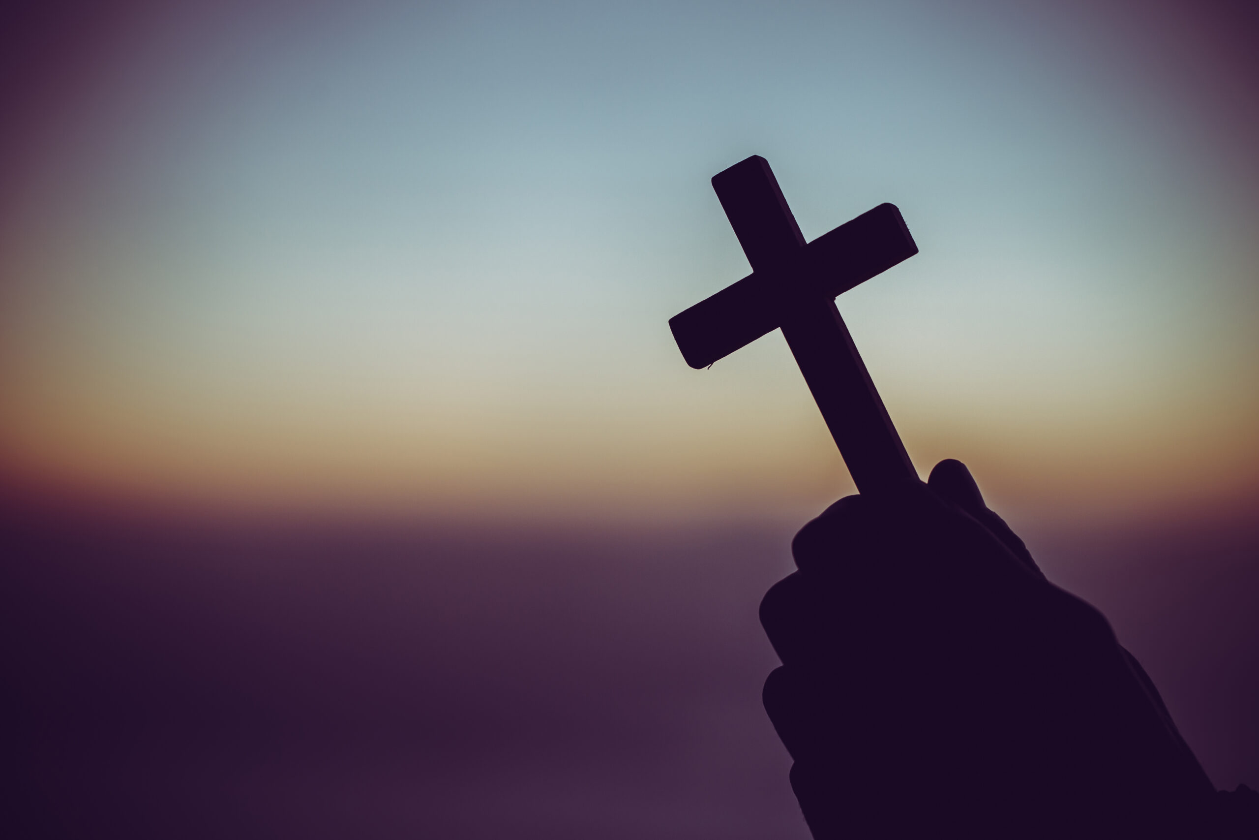 Silhouette of a man praying with a cross in hand at sunrise